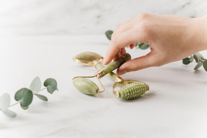 Hand holding jade facial rollers, the gua sha and face roller category